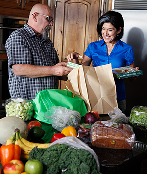 Man and woman taking groceries out of bags in kitchen.