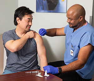 Healthcare provider giving man injection in upper arm in exam room.